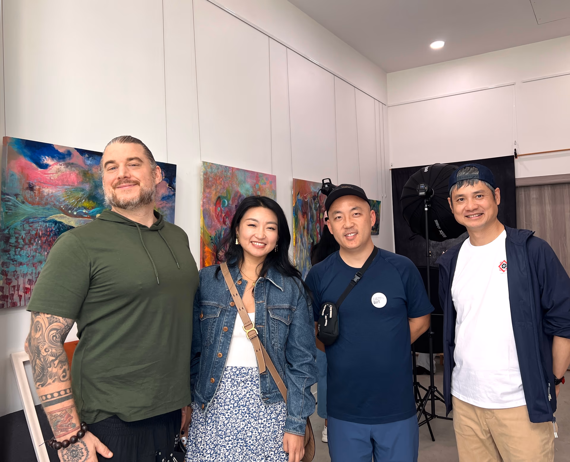 Four workshop participants smile together in the studio, in front of brightly coloured abstract paintings and a portrait backdrop.